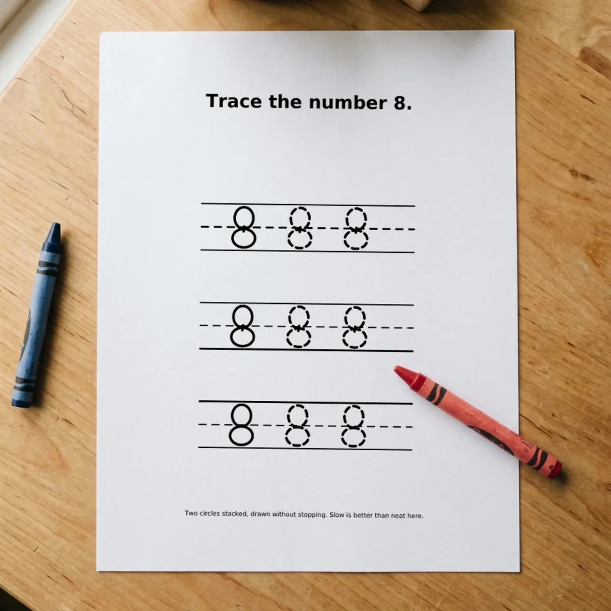 The Numbers & Counting page “Trace the number 8.” printed and lying on a wooden table, a red crayon across its corner.