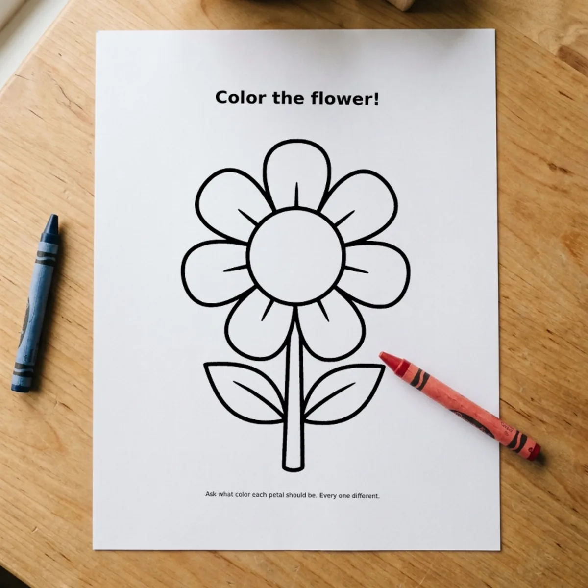 The Seek & Find page “Color the flower!” printed and lying on a wooden table, a red crayon across its corner.